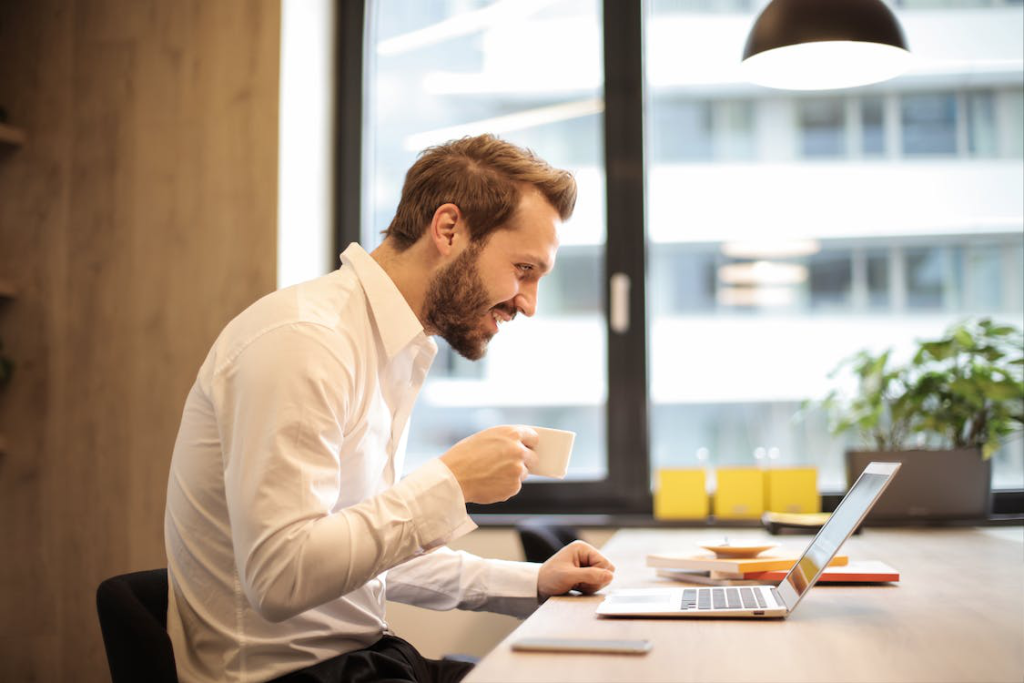 Man holding teacup in front of laptop on top of table inside the room