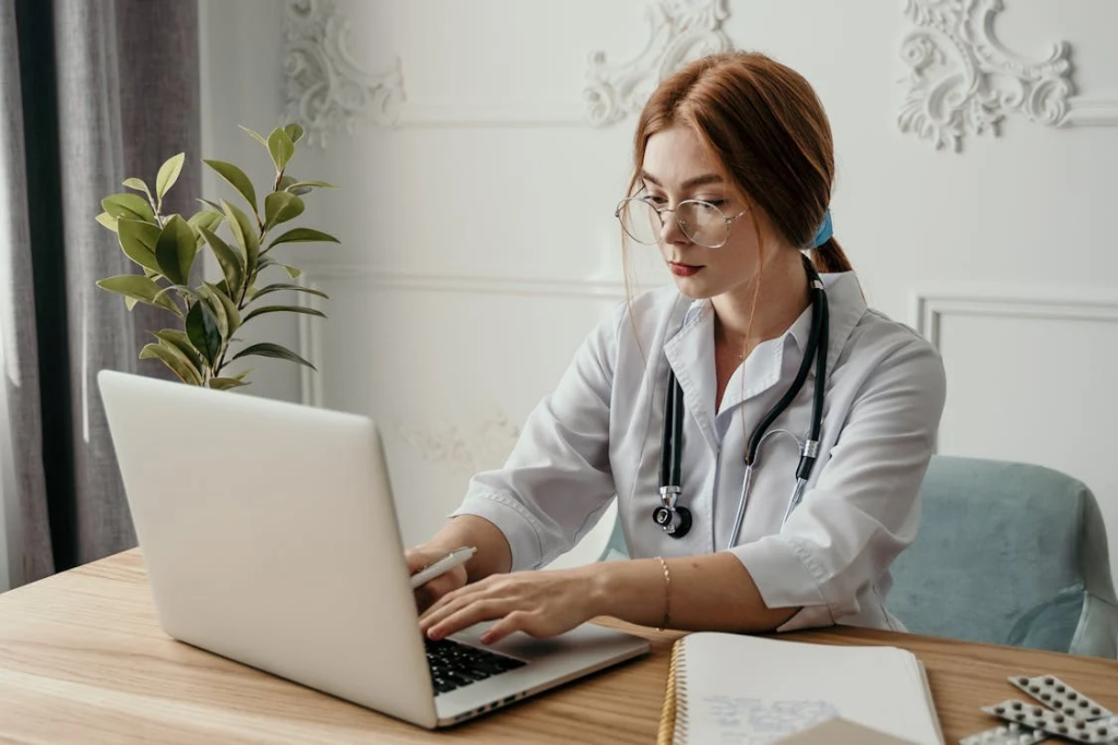 a medical professional using a laptop at their desk