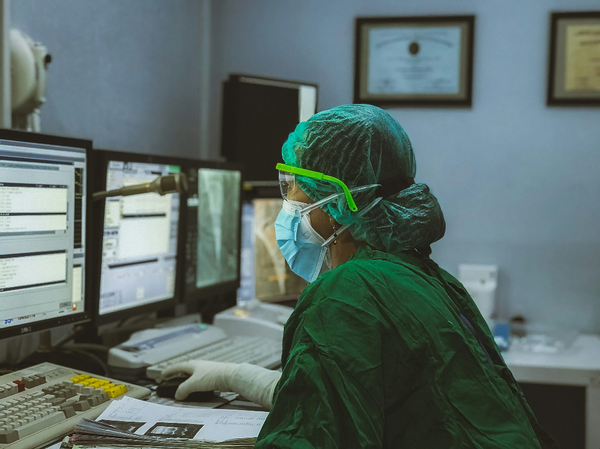 Healthcare worker in scrubs and a face mask looking at a computer monitor.